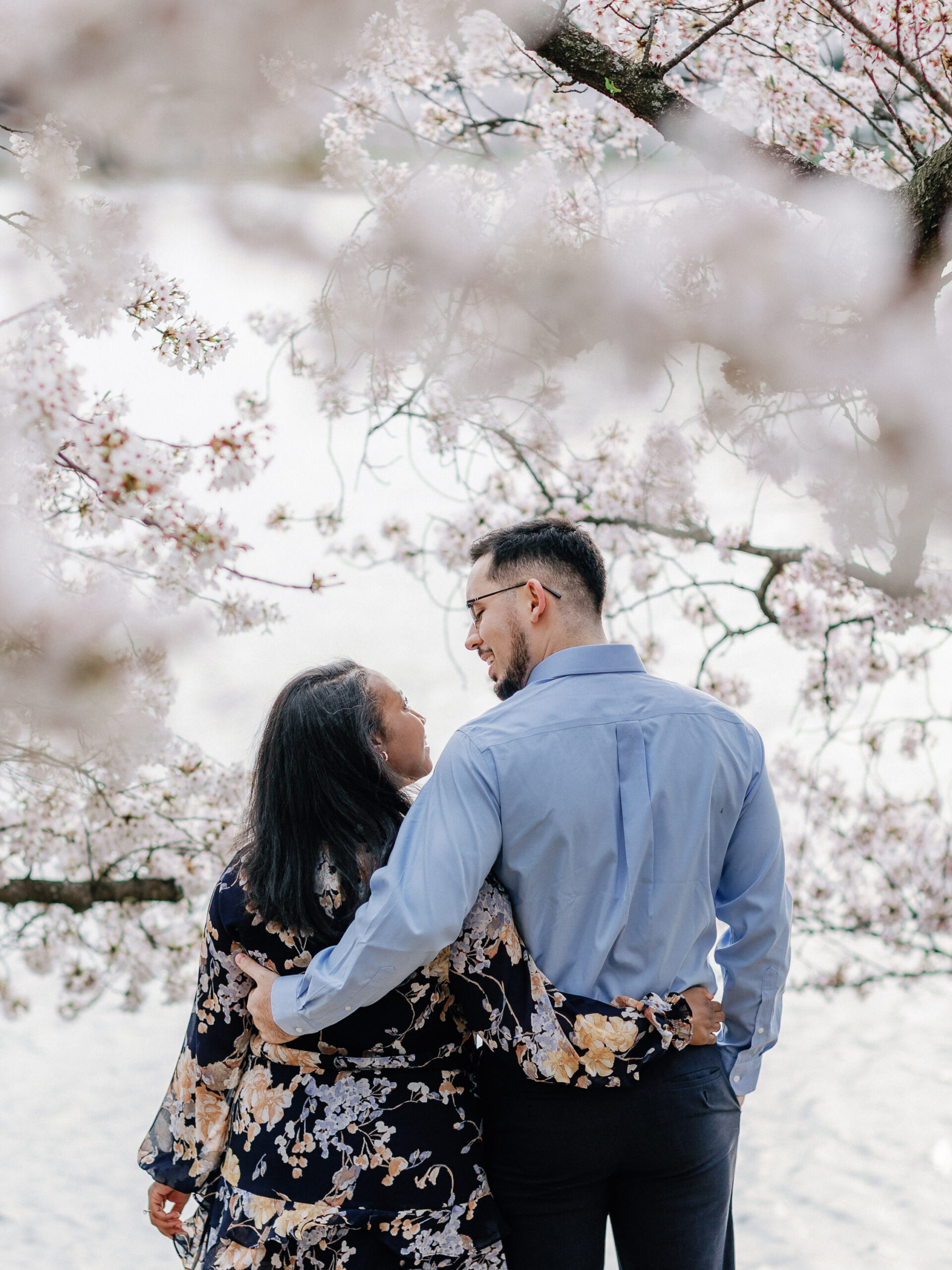 A newly engaged couple admiring each other underneath cherry blossom trees.