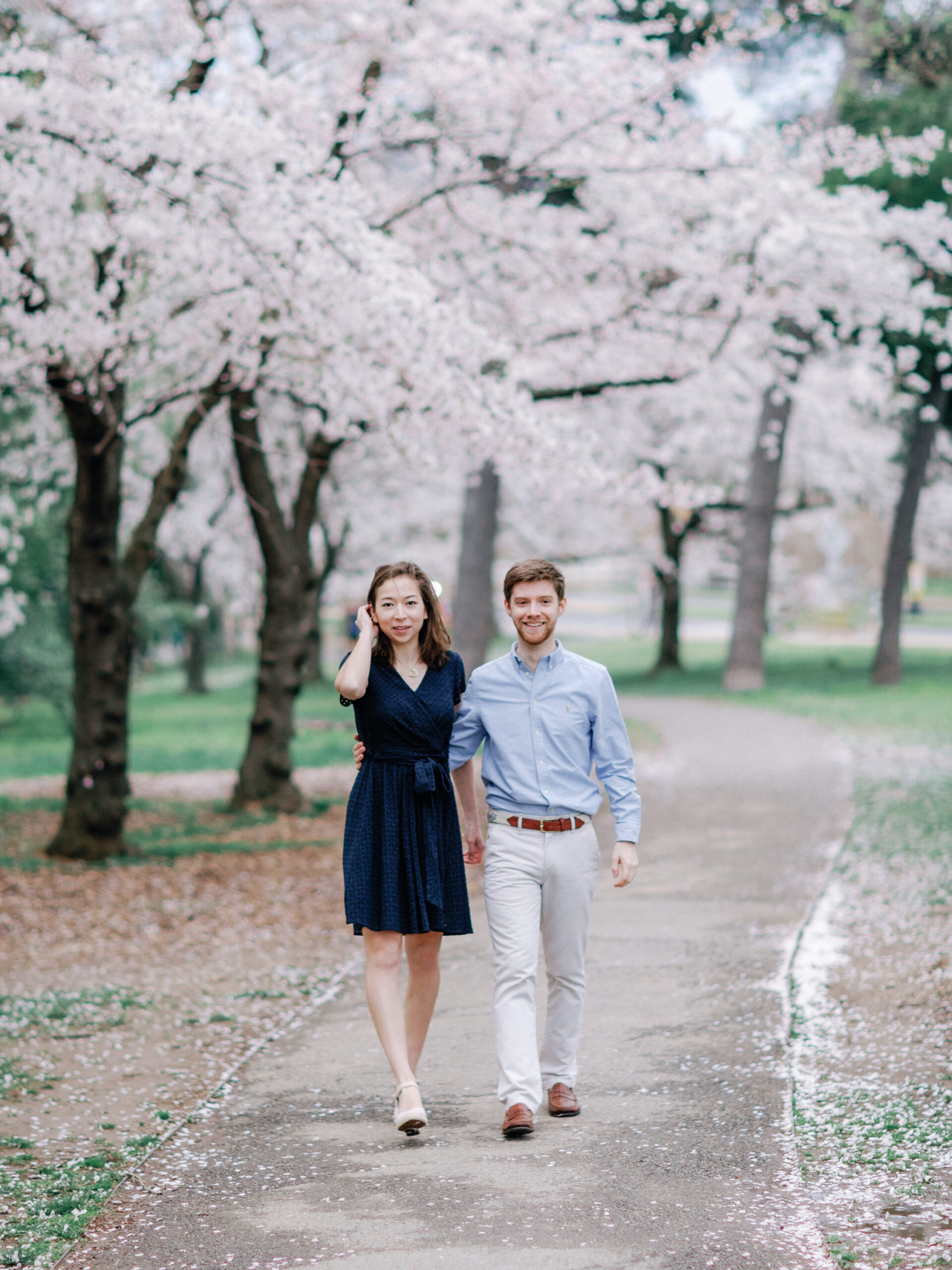 A newly engaged couple walking hand in hand underneath cherry blossom trees in full bloom.